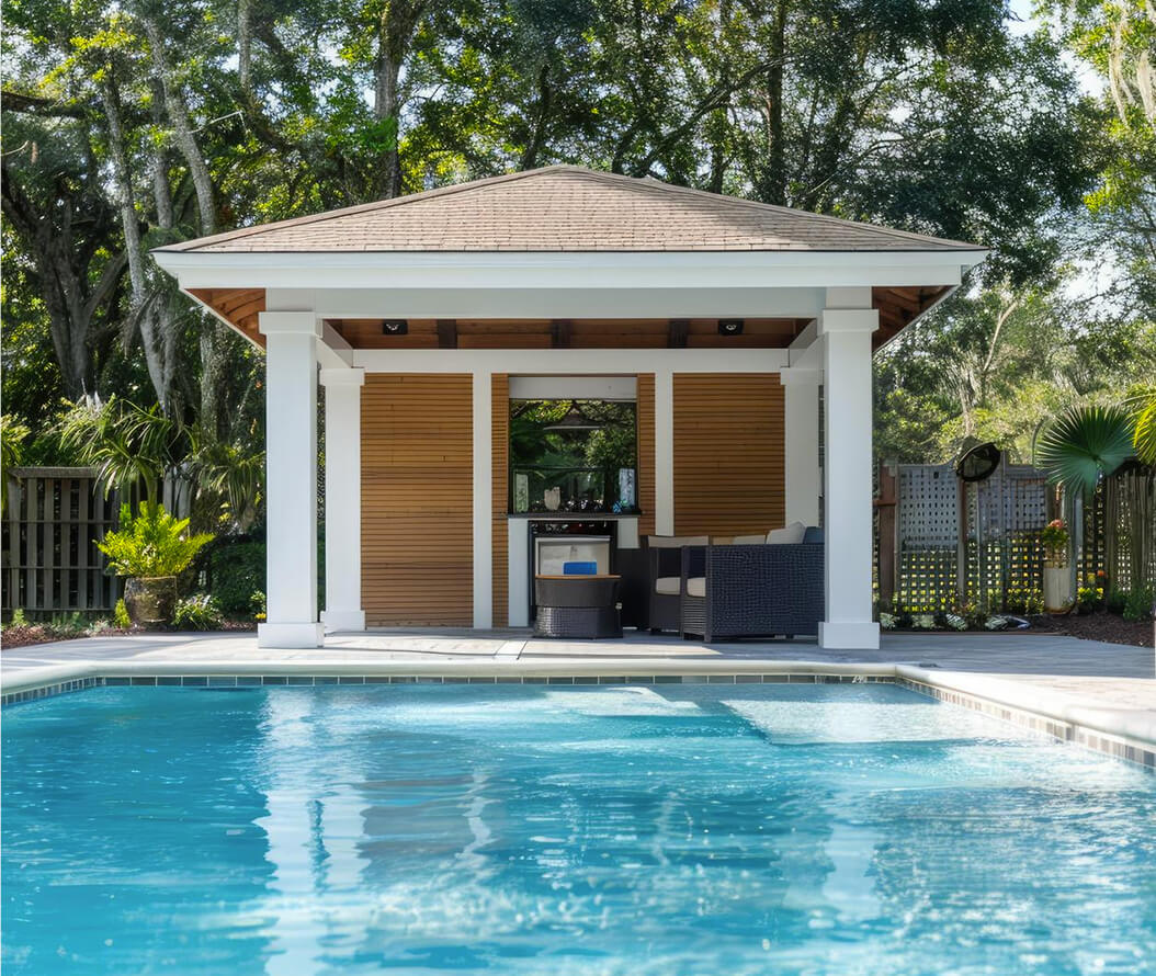 A charming pool house adjacent to a clear blue pool, set in a peaceful outdoor environment.